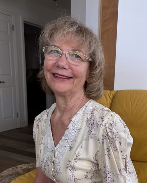 Patricia M. Keppler, reading specialist, smiling warmly in wire-rimmed glasses and a cream floral dress, seated in a yellow armchair